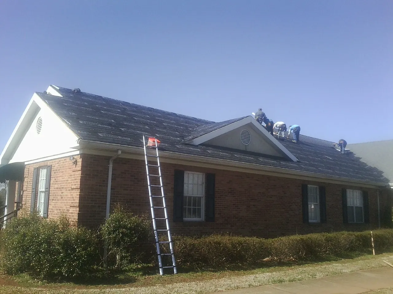 Crew tearing shingles off a brick ranch roof with a ladder set — Emergency Roof Repair work by our crew in Wallkill