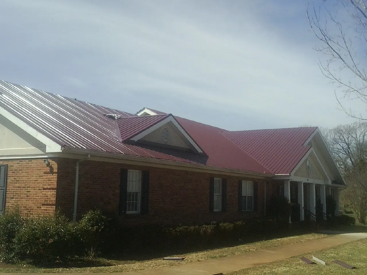 Red metal roof with gabled entries on a long brick building, from a Hail Damage Roof Repair job in Wallkill