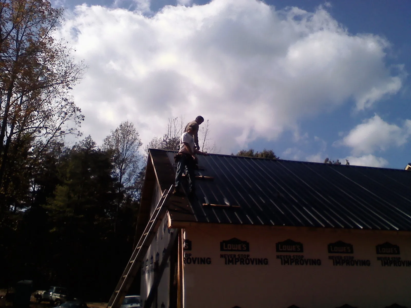 Roofer fastening dark metal panels high against a cloudy sky, from a Roof Inspection job in Wallkill